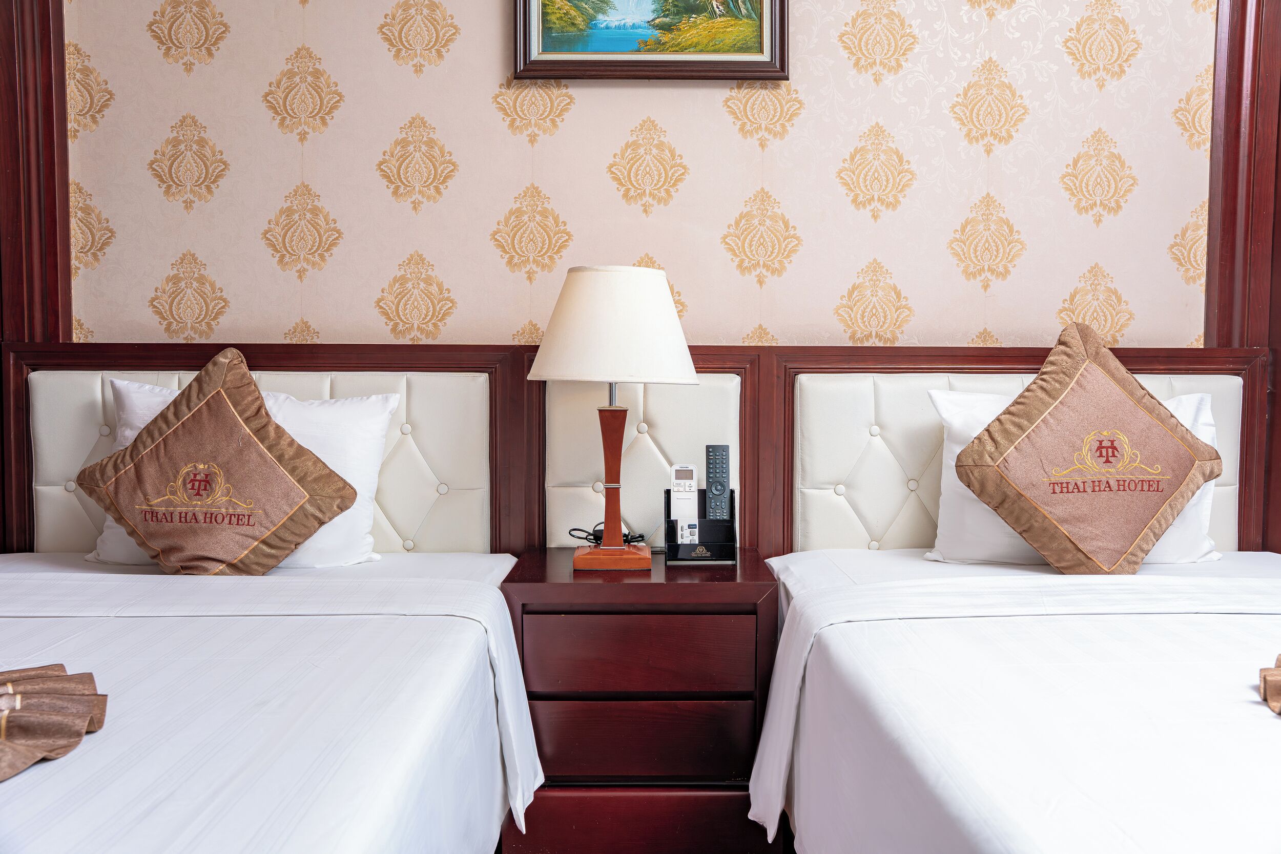 A hotel room with two beds, a nightstand with a lamp, and a wall with a patterned wallpaper.