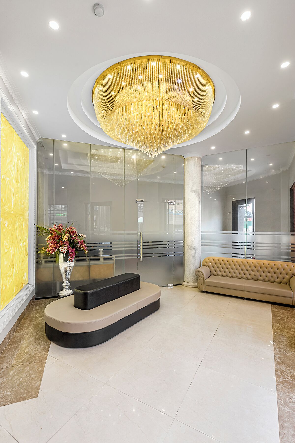 A modern lobby with a central chandelier, a reception desk, a sofa, and a glass wall.