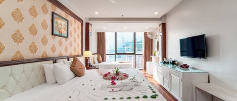 A hotel room with a large bed, a TV, a desk with a lamp, and a view of the city.