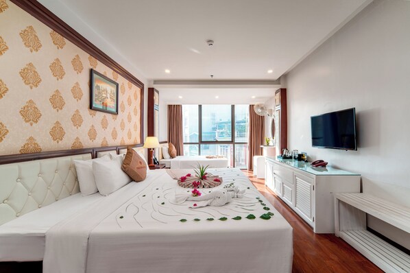 A hotel room with a large bed, a TV, a desk with a lamp, and a view of the city. - Thai Ha Hotel (Bai Chay)