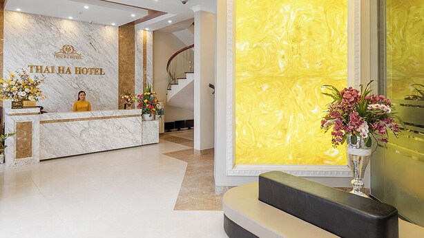 A modern hotel lobby with a reception desk, a large chandelier, and a marble wall with a yellow pattern. - Thai Ha Hotel (Bai Chay)