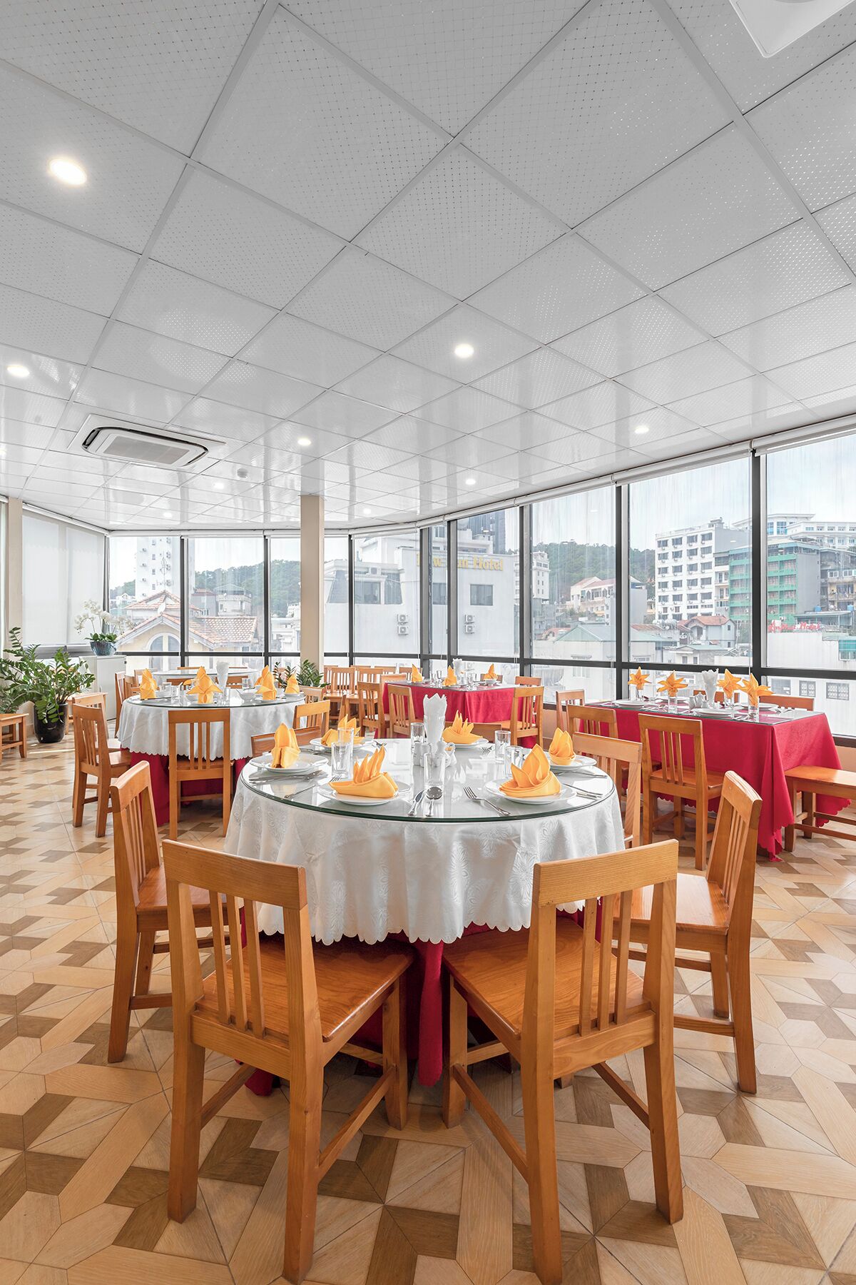 Un comedor amplio con mesas redondas, sillas de madera y vistas a la ciudad a través de ventanas grandes.