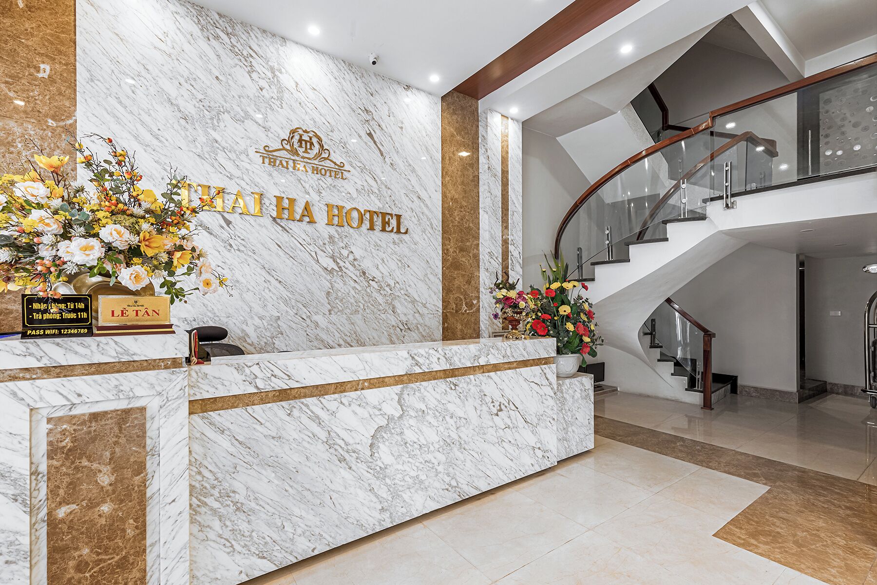 A hotel reception desk with a marble counter, a staircase, and a sign reading "THAI HA HOTEL".