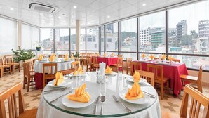 A restaurant with round tables set for dining, large windows offering city views, and a tiled floor. - Thai Ha Hotel (Bai Chay)