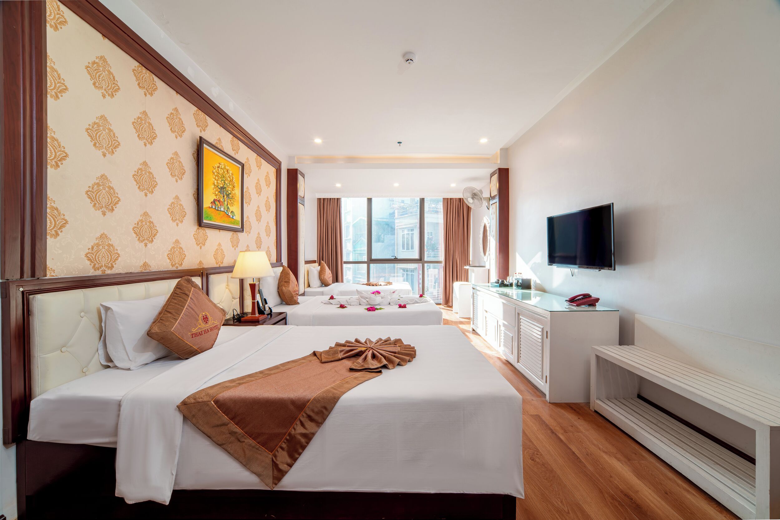 A hotel room with two beds, a TV, a desk, and a window with a view.