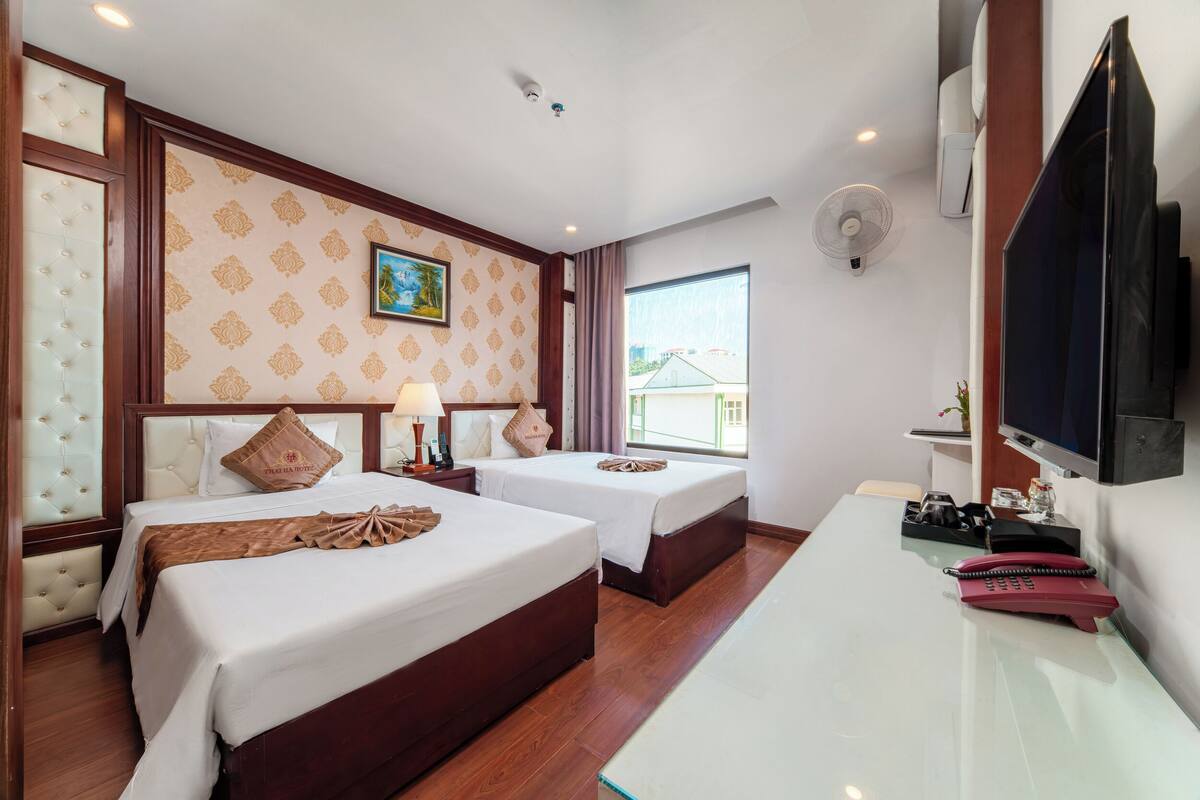 A hotel room with two beds, a desk, a TV, and a window with a view.