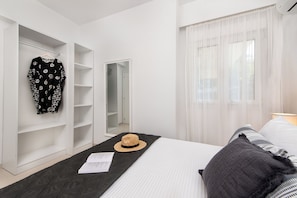 Hotellihuone, jossa on sänky, vaatekaappi, peili ja ikkuna, jossa on ohuet verhot.