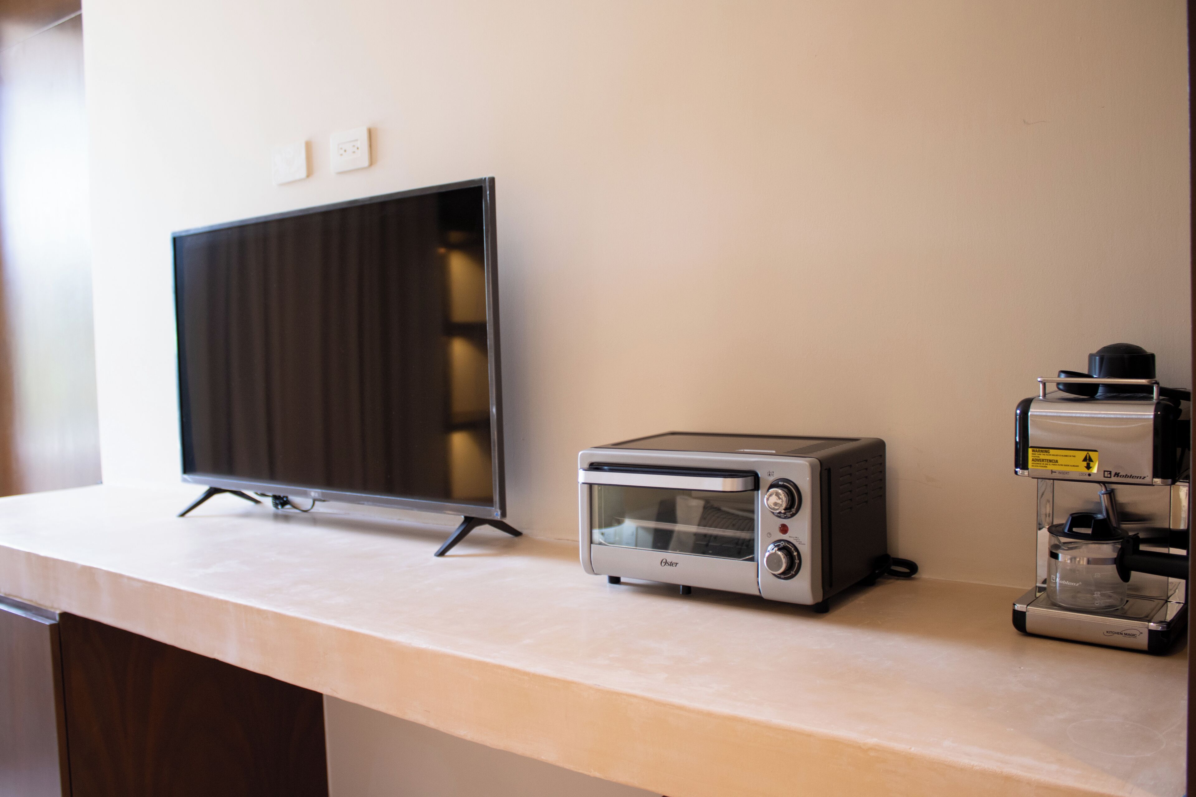 A kitchen counter with a flat-screen TV, a toaster oven, and a coffee machine.