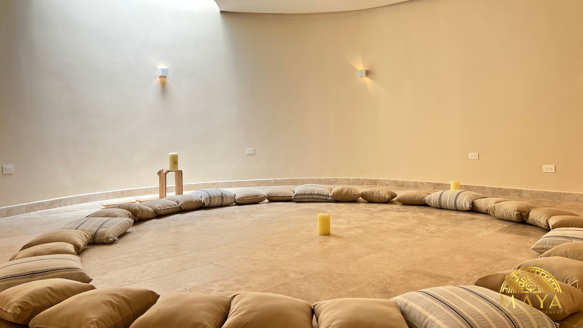 Un espacio de descanso circular con cojines y velas, un atril de madera y luces fijadas a la pared.