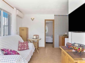 Une chambre avec un lit, une petite table sur laquelle est posée une bougie, une télévision et un panier décoratif.
