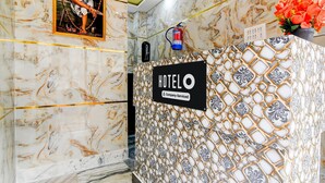 Een hotel receptie met een marmeren wand, een ingelijste foto van een persoon, een brandblusser en een bordje waarop staat dat het hotel bedrijfsmatig wordt beheerd.