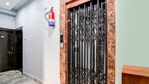 Een gang met een metalen poortdeur, een brandblusser aan de muur en een houten bankje.