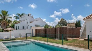 Una piscina con agua cristalina azul, rodeada por una zona vallada y un edificio blanco al fondo.
