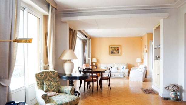 Ein geräumiges Wohnzimmer mit Holzboden, einem gemusterten Sessel, einem runden Tisch mit Stühlen, einer Couch und einem Bild an der Wand.