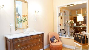 Ein Badezimmer mit einem Holzkosmetikschrank, einem Spiegel und einem Fenster mit Blick auf einen Raum, der Regale und eine Lampe enthält.