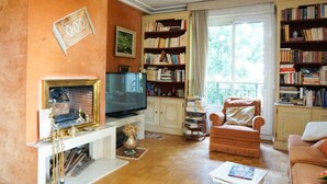 Ein Wohnzimmer mit Kamin, Fernseher, Bücherregalen und einer gemütlichen Sitzecke.
