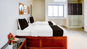 A hotel room with a bed, a desk with a telephone, a vase with flowers, a ceiling fan, and a window with curtains. - Super Hotel O Pachgaon (Kolhapur)