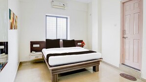 A bedroom with a bed, bedside table, nightstand, window, air conditioning unit, and a door. - Super Hotel O Pachgaon (Kolhapur)