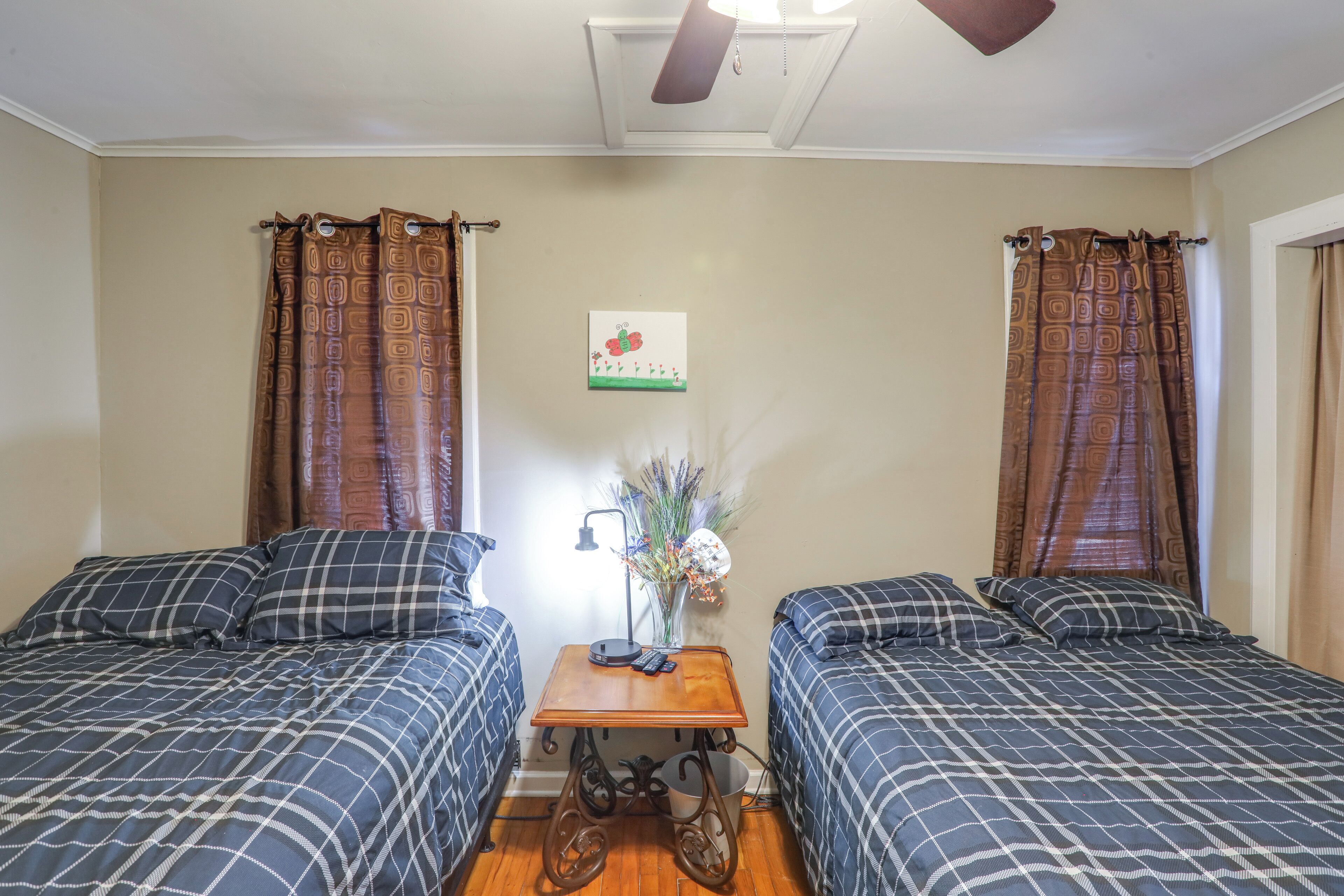 A room with two beds, a small table with a lamp, and a wall decoration.