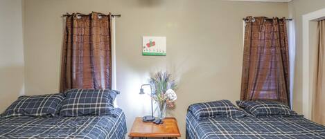 A room with two beds, a small table with a lamp, and a wall decoration.