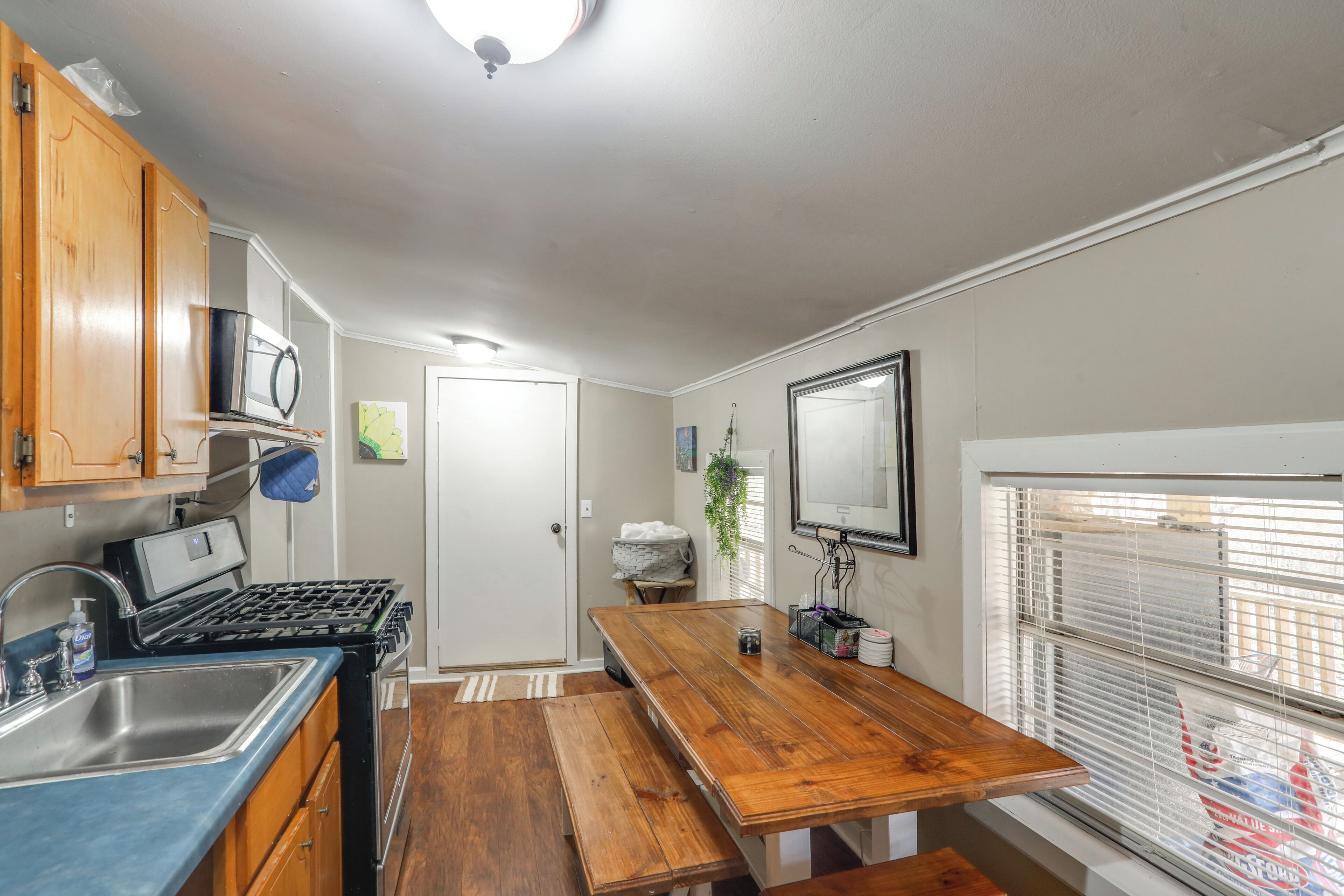 A compact kitchen with wooden cabinets, a built-in microwave, a stove, a sink, and a window with blinds.