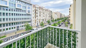 A modern urban street with multi-story buildings, a clear sky, and a balcony with a metal railing. - New Big Flat 8 Pers AC WiFi (Nice)