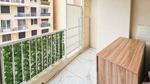 A balcony with a metal railing, a wooden cabinet, and a view of a building with multiple balconies. - New Big Flat 8 Pers AC WiFi (Nice)