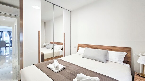 A modern hotel room with a large bed, a wooden headboard, and a large mirror. - New Big Flat 8 Pers AC WiFi (Nice)