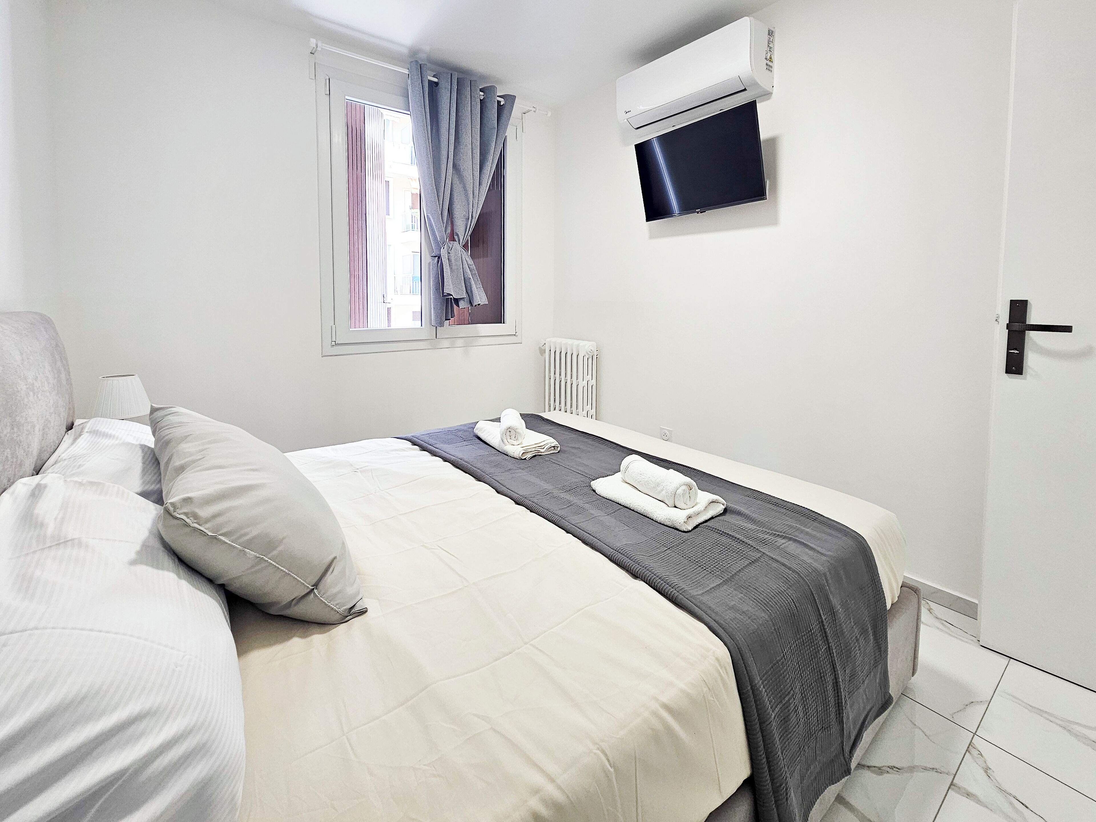 A hotel room with a bed, a TV mounted on the wall, and a window with curtains.