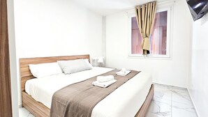 A neatly made bed with white linens and a brown throw blanket, a wooden headboard, and a window with curtains. - New Big Flat 8 Pers AC WiFi (Nice)