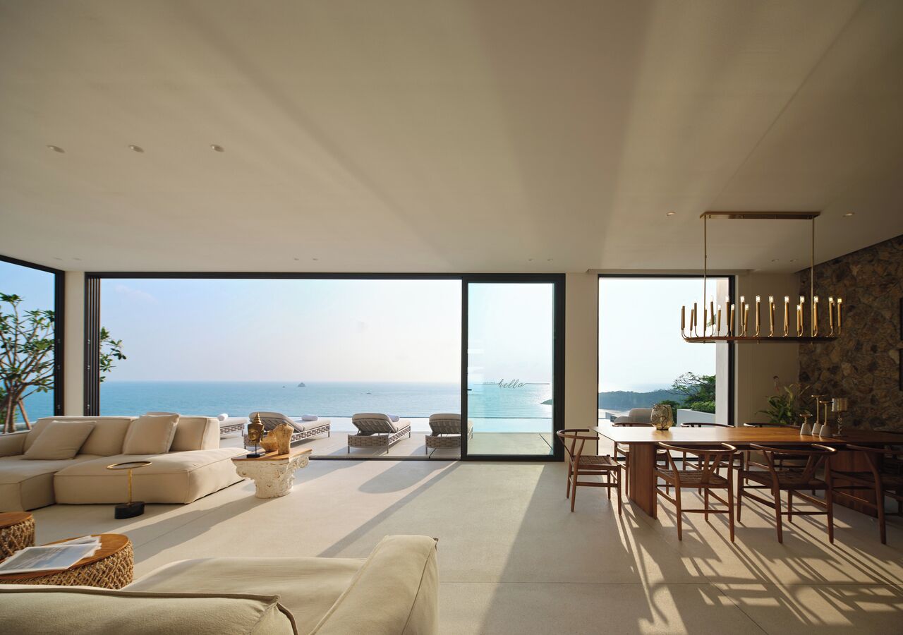 A spacious living area with a large window overlooking the sea, a dining area with a wooden table and chairs, and a modern interior design.