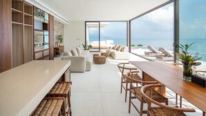 Un espacio moderno de estar con cocina, comedor y un amplio ventanal con vistas al mar.
