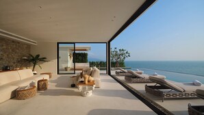 Un salón moderno con un amplio ventanal que da a un balcón con vistas al mar.