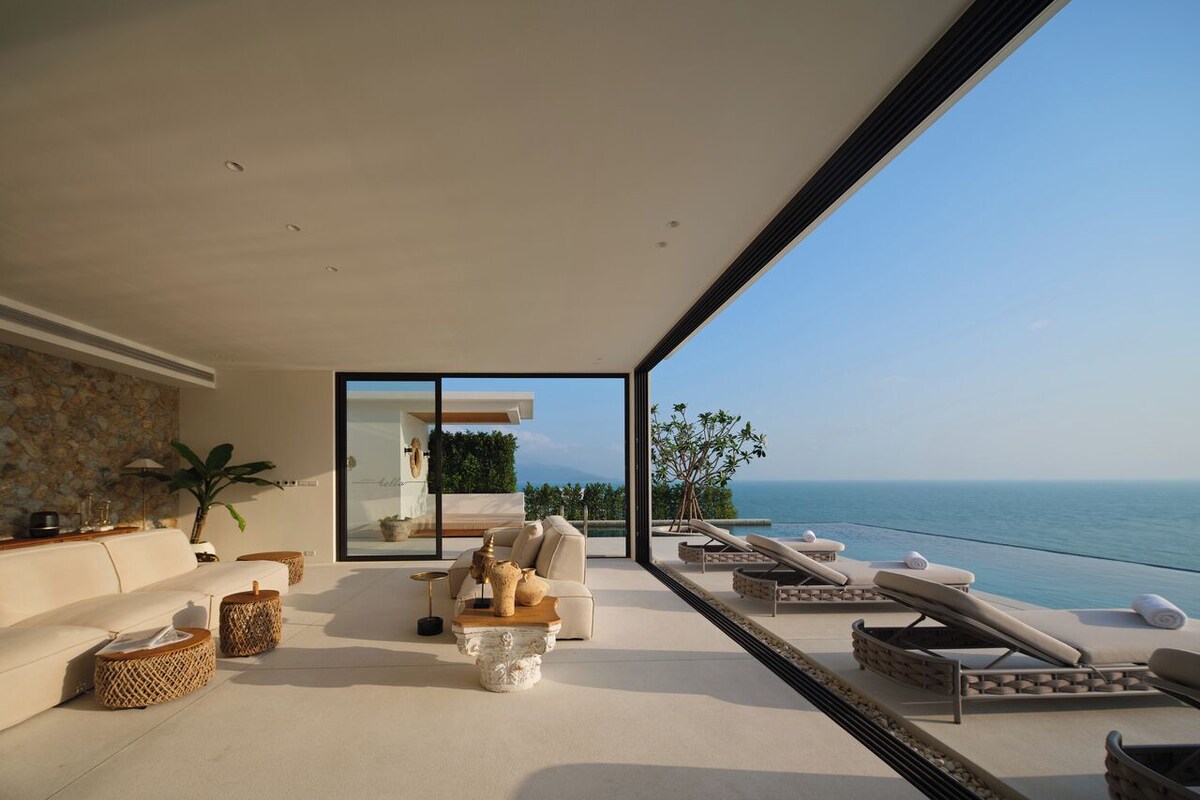 A modern living room with a large glass door leading to a balcony overlooking the sea.