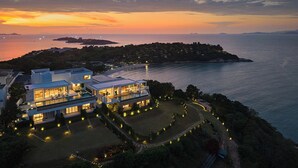 Una casa moderna de dos plantas con un balcón grande, rodeada de un jardín ajardinado, con vistas a la costa.