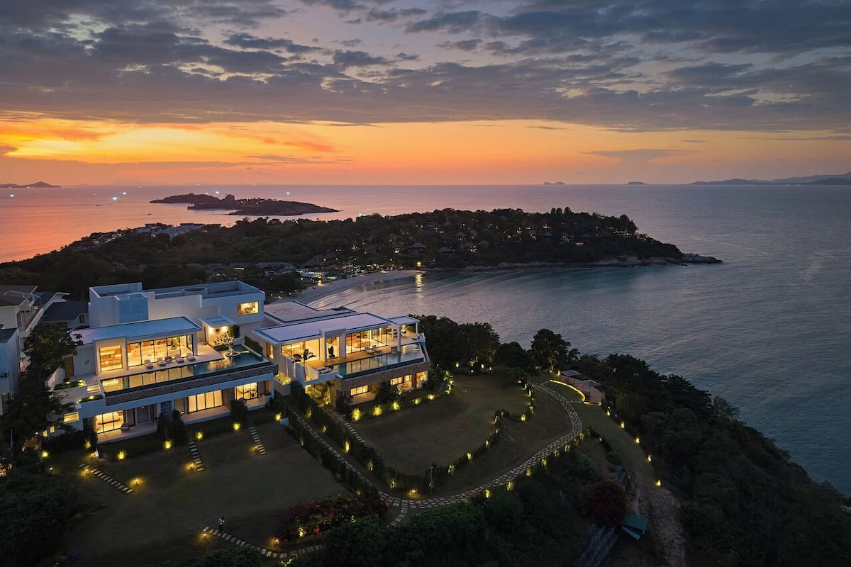 Une maison moderne à deux étages, dotée d’un grand balcon, entourée d’un jardin aménagé et offrant une vue sur la côte.