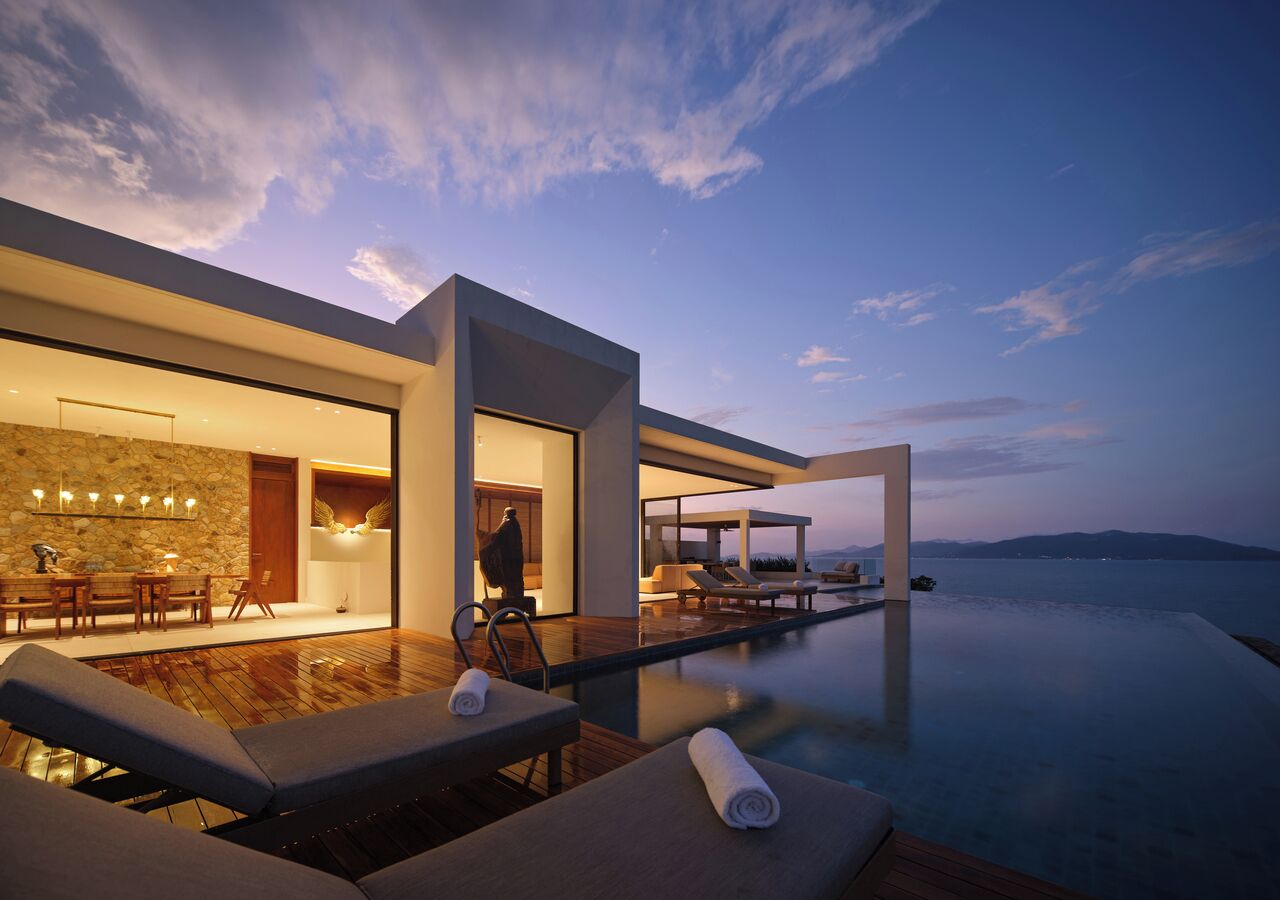 A modern infinity pool with lounge chairs and a dining area.