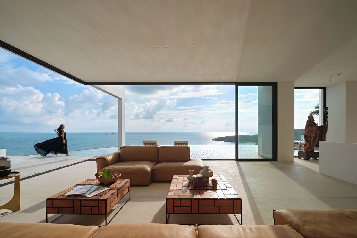 A spacious living area with a large window overlooking the sea, a leather sofa, and a coffee table.