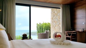 Habitación de hotel con una cama grande, vista al mar, pared de piedra y un escritorio de madera.