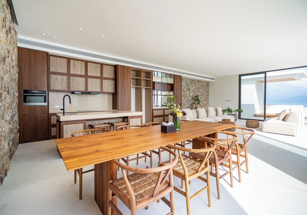 Une cuisine moderne avec une table et des chaises en bois, un four encastré et une grande fenêtre donnant sur l’océan.