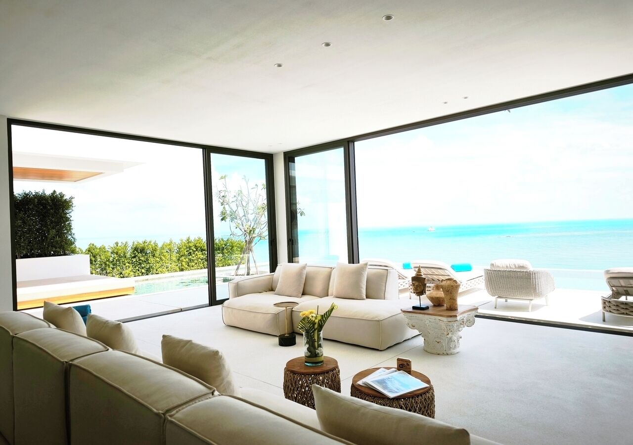 A modern living room with a large sofa, a coffee table, and a side table. There is a view of the ocean through large windows.