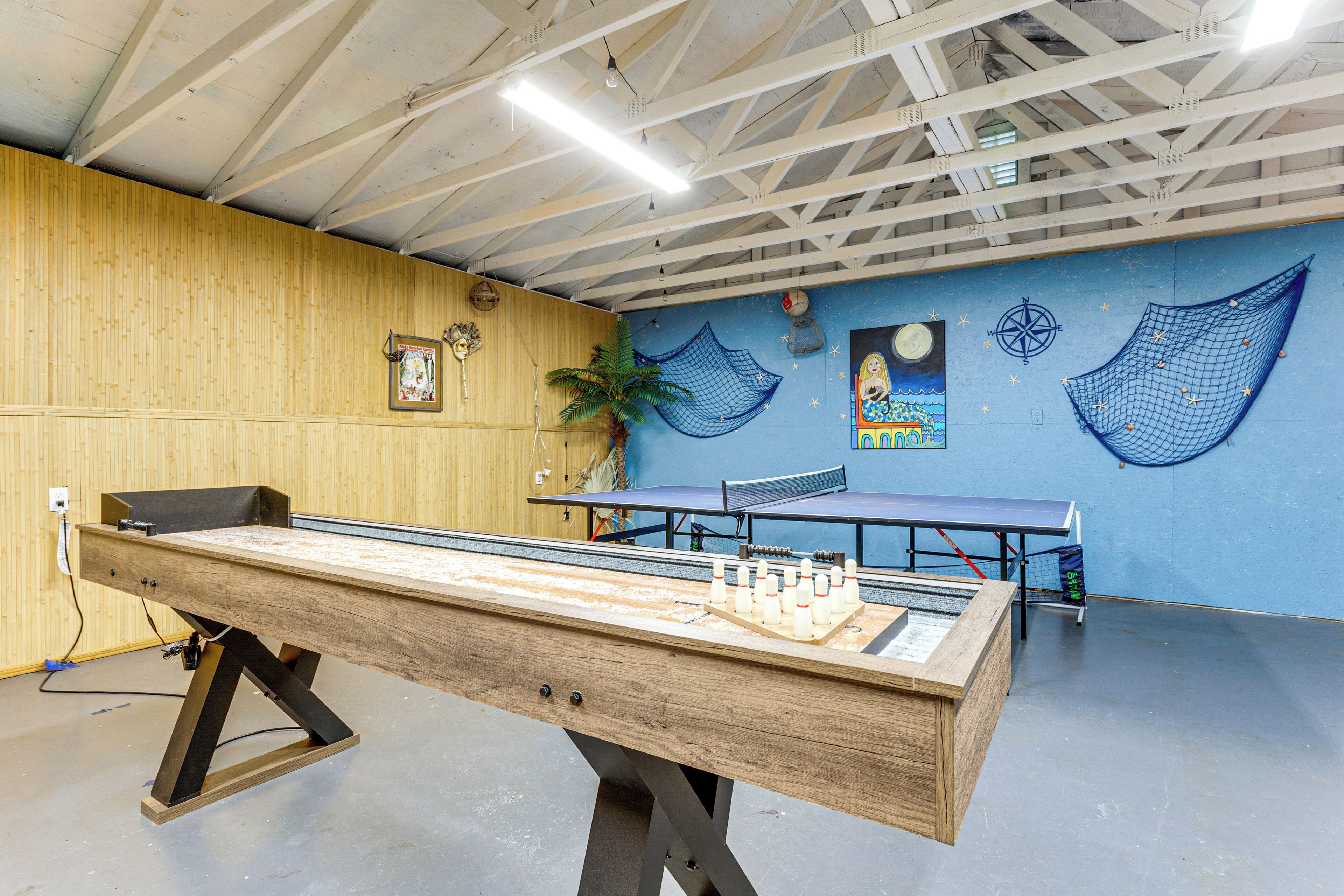Una mesa de ping pong en una habitación con pared azul, paneles de madera y techo con vigas a la vista.