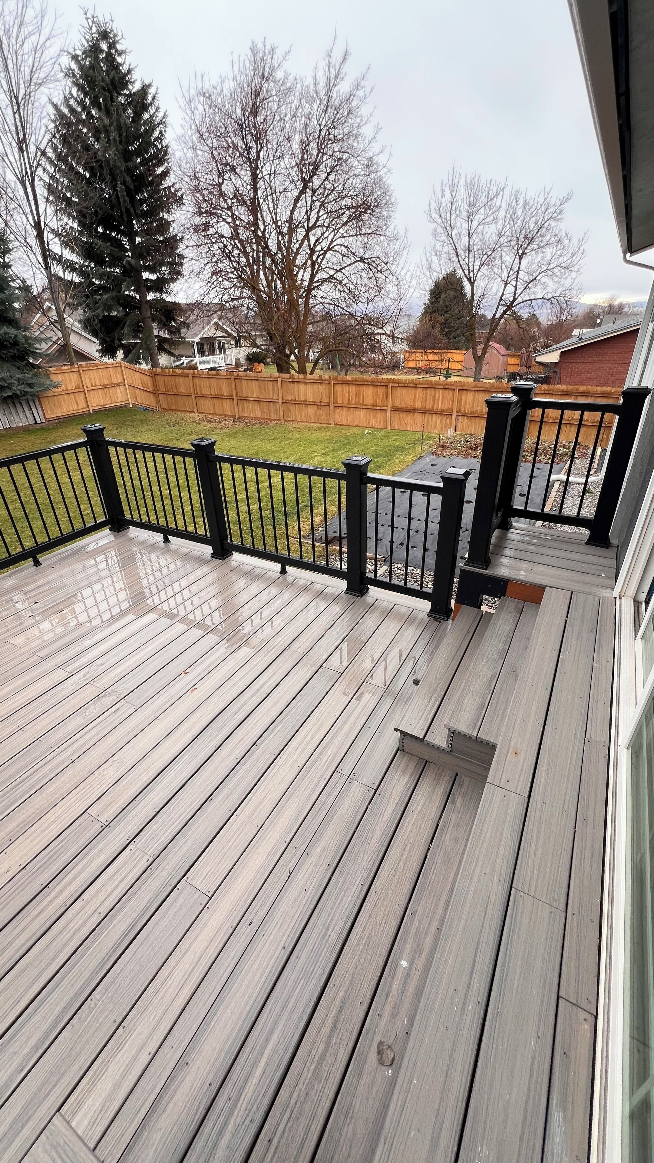 A wooden deck with a black railing, surrounded by a wooden fence and trees.