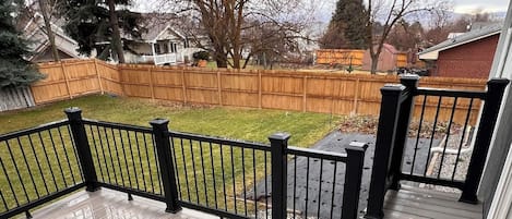 Une terrasse en bois avec une rambarde noire, entourée d’une clôture en bois et d’arbres.