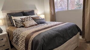 Une chambre à coucher avec un lit, des tables de chevet, une fenêtre avec des rideaux et un luminaire au plafond.