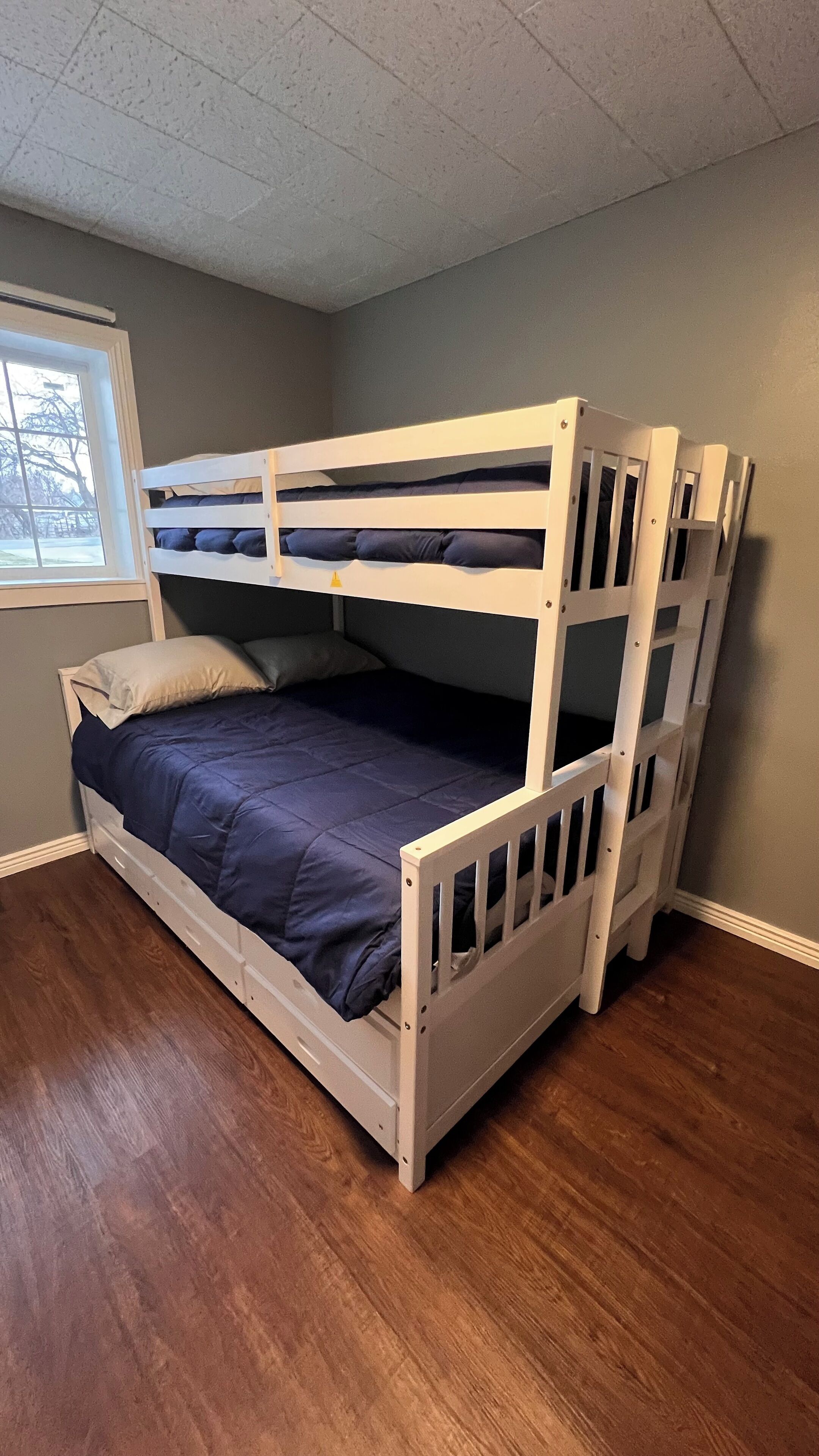 Een stapelbed in een kamer met houten vloeren en een raam.