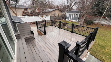 A wooden deck with a black railing, a white picket fence, and a house in the background.