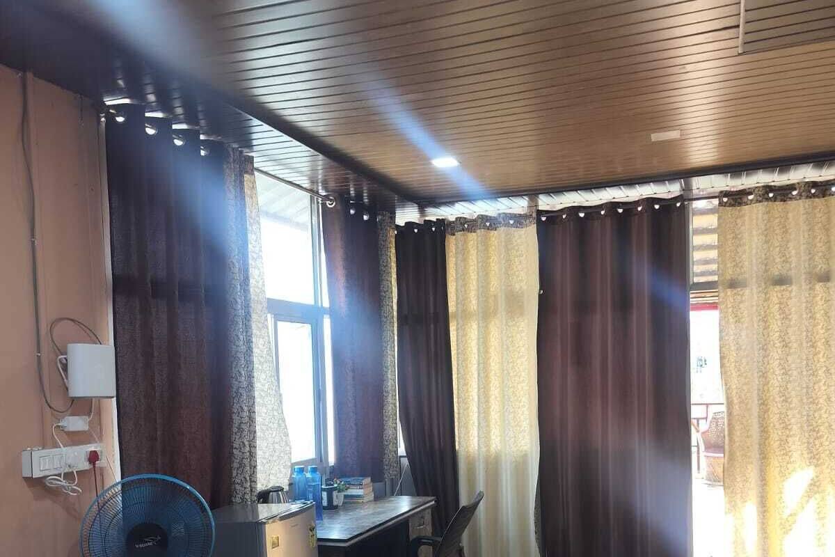 A room with a desk, chair, fan, and a patterned rug.