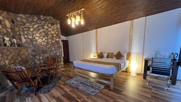 A bedroom with a stone wall, wooden floor, a bed, a desk, and a chair. - Adaara - A Pet Friendly Cottage (Almora)