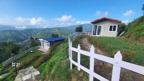 A hillside view of a property with a white picket fence, a red-roofed building, and a blue-roofed structure.